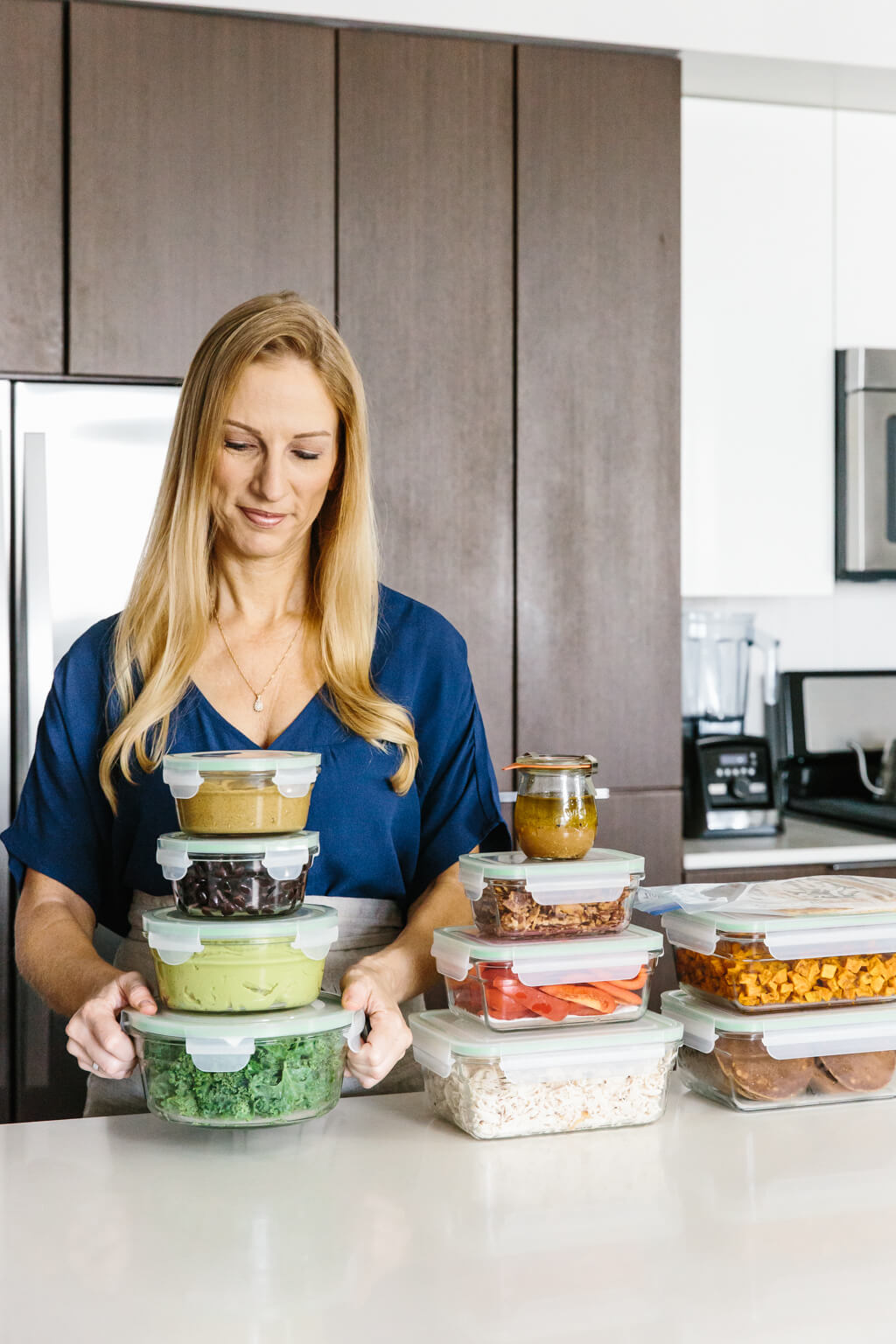 Girl standing with a stack of ingredients in meal prep containers. 