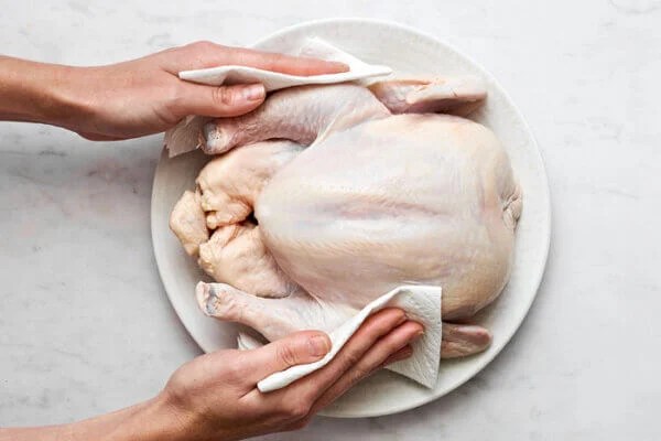 A raw whole chicken on a plate before roasting