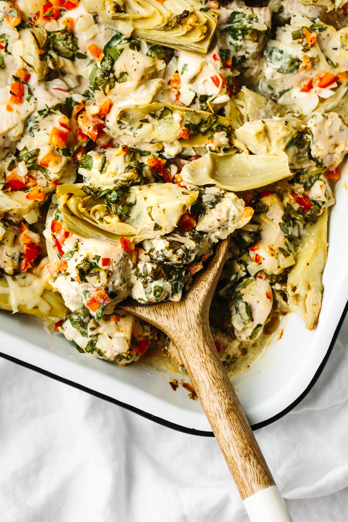 A wooden spin digging into a spinach artichoke chicken bake