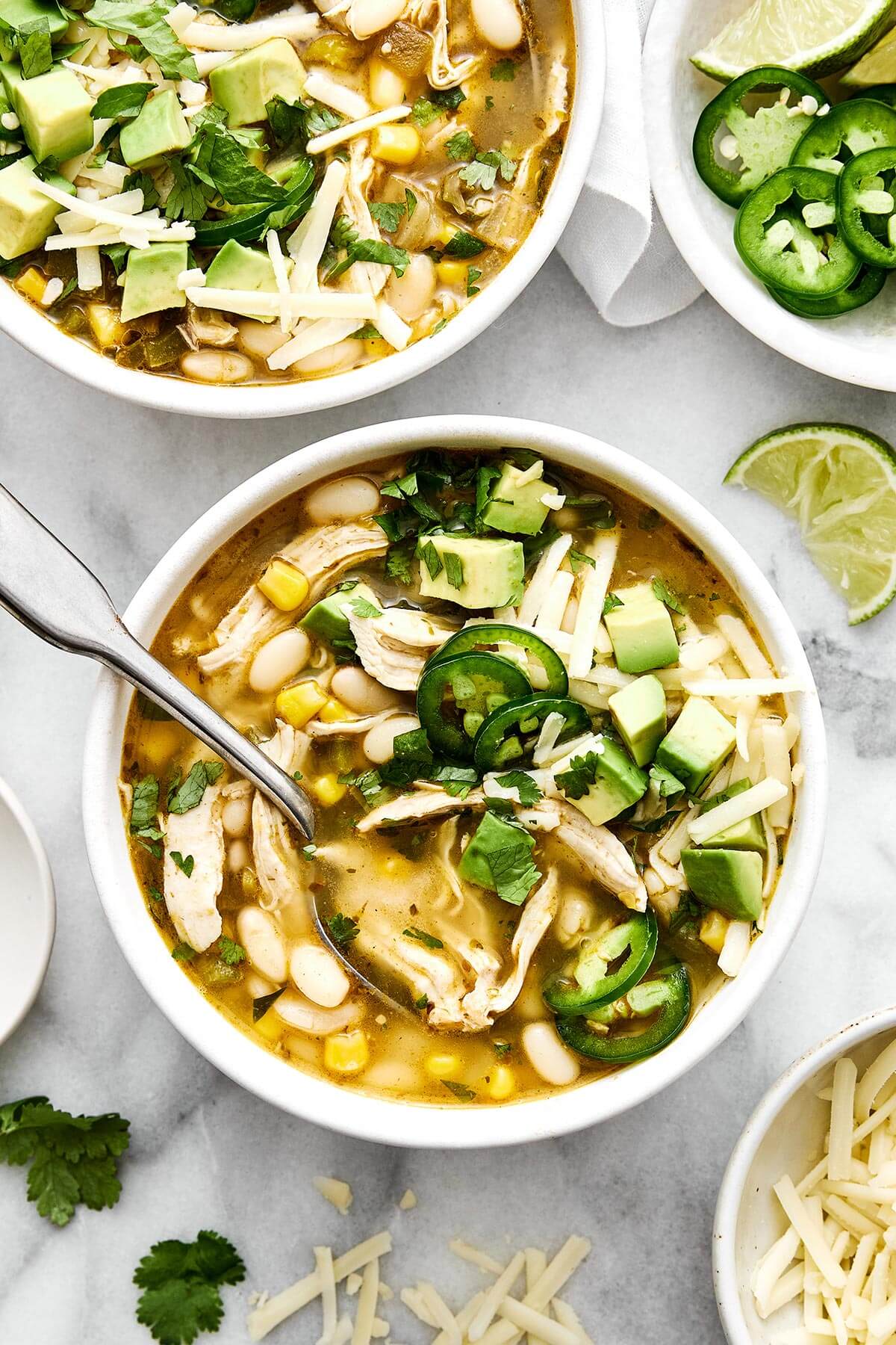 This white chicken chili is a fall/winter comfort food favorite and a flavorful blend of tender chicken, white beans, sweet corn, green chiles, and more! Bowls of white chicken chili.