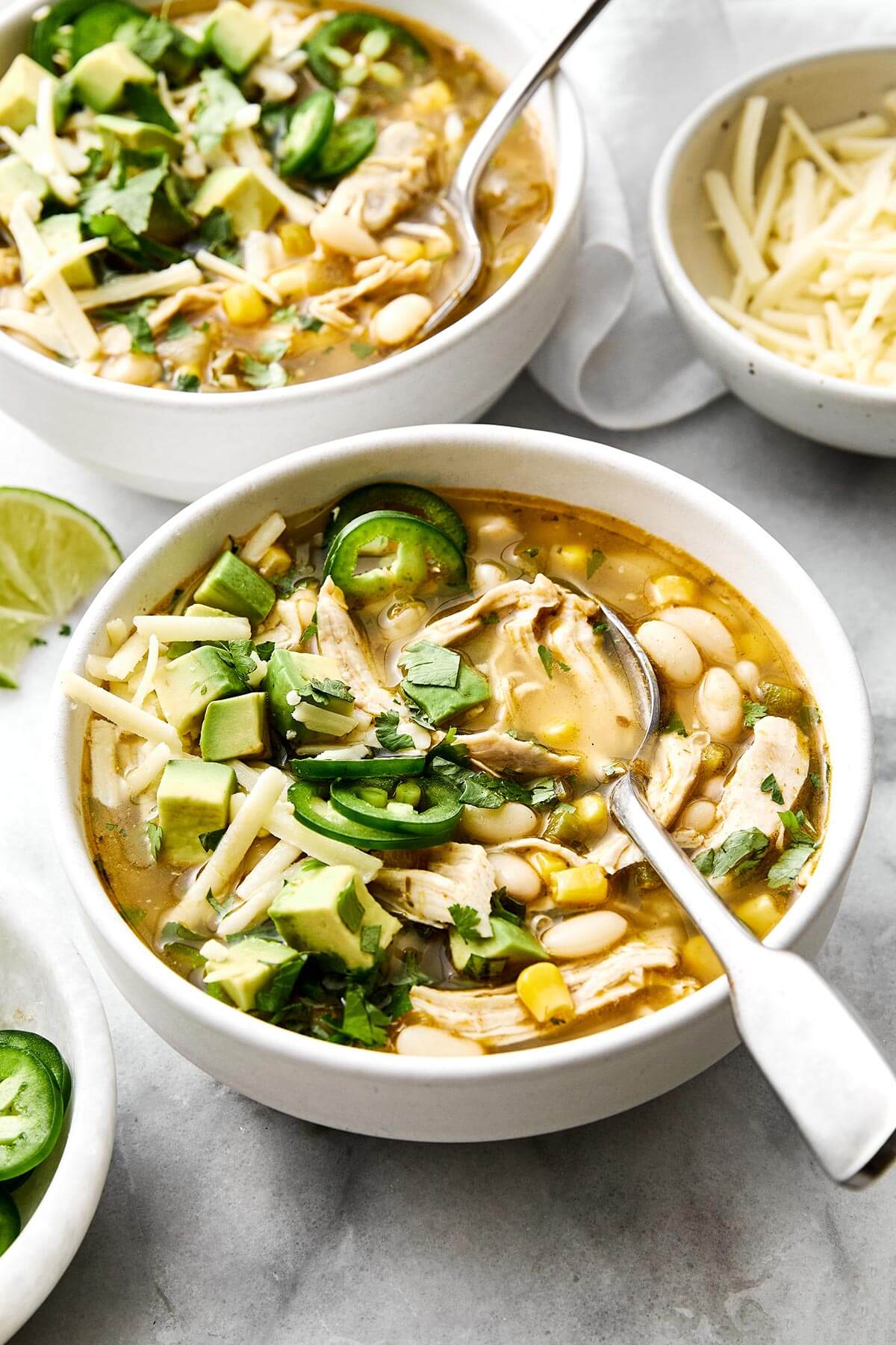This white chicken chili is a fall/winter comfort food favorite and a flavorful blend of tender chicken, white beans, sweet corn, green chiles, and more! Bowl of white chicken chili and a spoon.